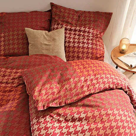 Bettwäsche in warmen Herbsttönen mit elegantem Hahnentrittmuster schmückt das Schlafzimmer.