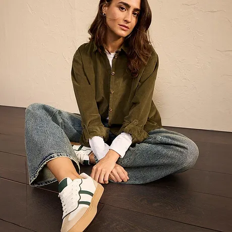 Olivgrüne Jacke mit Jeans und weiße Sneaker mit grünen Streifen.