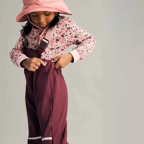 Look coloré pour les filles : pull rose à petites fleurs, pantalon de pluie bordeaux et chapeau en couleur pastel.