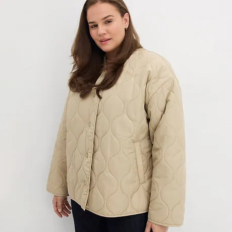 Beige Steppjacke mit Knöpfen, kombiniert mit dunkler Hose.