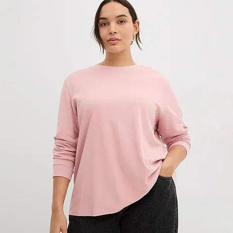 Ein zartrosa Langarmshirt mit Rundhalsausschnitt ergänzt die dunkle Hose perfekt.
