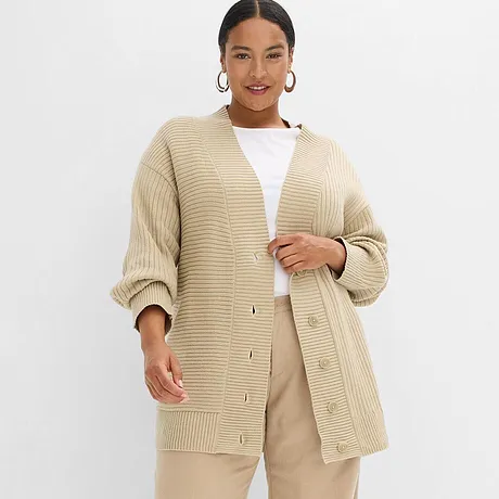 Beiger Oversize-Cardigan aus grobem Strick, kombiniert mit weißem Top und hellbeiger Hose.