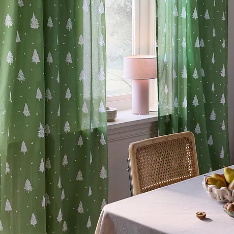 Des rideaux festifs de couleur verte avec des sapins blancs décorent la fenêtre.