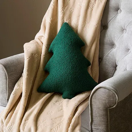 Fauteuil avec plaid couleur crème et coussin vert en forme de sapin.