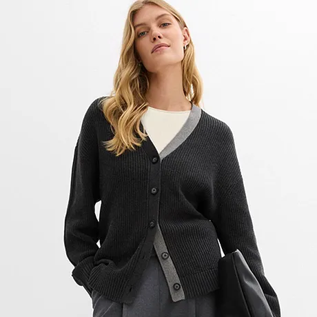 Gilet en maille foncé sur un T-shirt blanc, associé à une jupe grise et un sac noir.