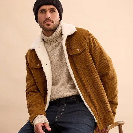 Pull en maille beige, veste en velours côtelé marron avec col en matière douillette et jean foncé.