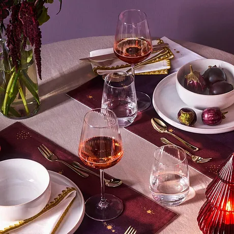Une vaisselle élégante et des couverts de couleur dorée décorent la table dressée pour les fêtes avec une nappe de couleur rouge bordeaux.