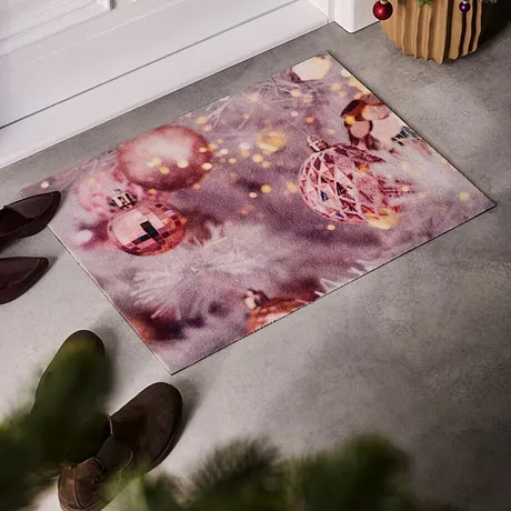 Tapis de protection festif avec de jolis motifs rose, une paire de chaussures et un petit sapin de Noël déposés à côté.