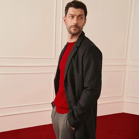 Manteau gris élégant sur un pull rouge, associé à un pantalon gris assorti.