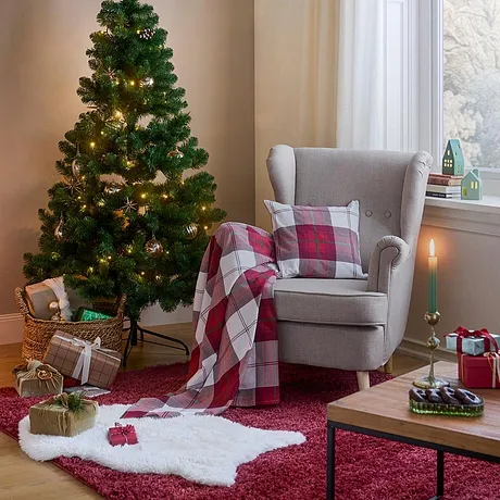 Une couverture à carreaux est déposée sur le fauteuil près du sapin de Noël et du tapis moelleux.