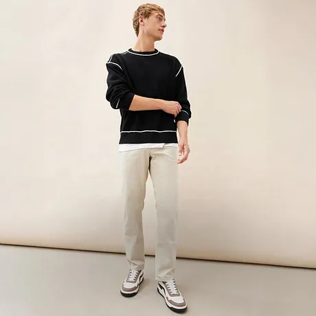 Look décontracté avec pull noir, pantalon clair et baskets.