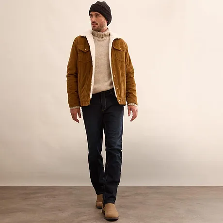 Veste marron, pull à col roulé couleur crème et jean foncé.