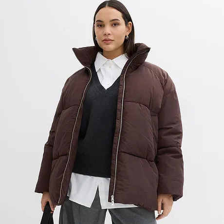 Veste d'hiver marron à col montant, pull foncé et chemise blanche en dessous.