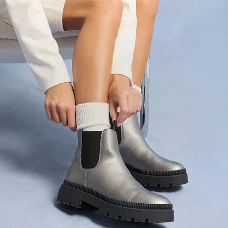 Weiße Socken und silberne Chelsea-Boots kontrastieren mit dem cremefarbenen Pullover.