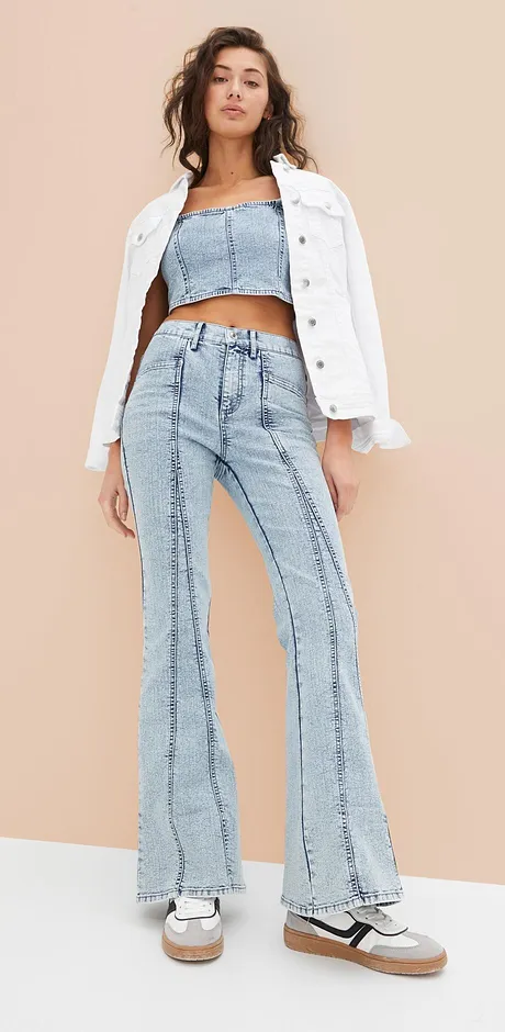 Trendiges Outfit mit weißer Jeansjacke, bauchfreiem Top und ausgestellter Jeans im Retro-Look.