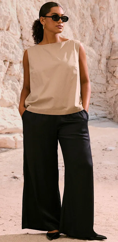 Tenue composée d'un top beige sans manches et d'un pantalon large noir. Des lunettes de soleil stylées finalisent le look.