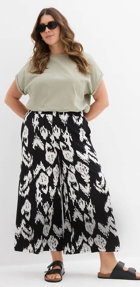 Olivgrünes T-Shirt, schwarz-weißer Maxirock mit Blumenmuster, Sonnenbrille und flache Sandalen.