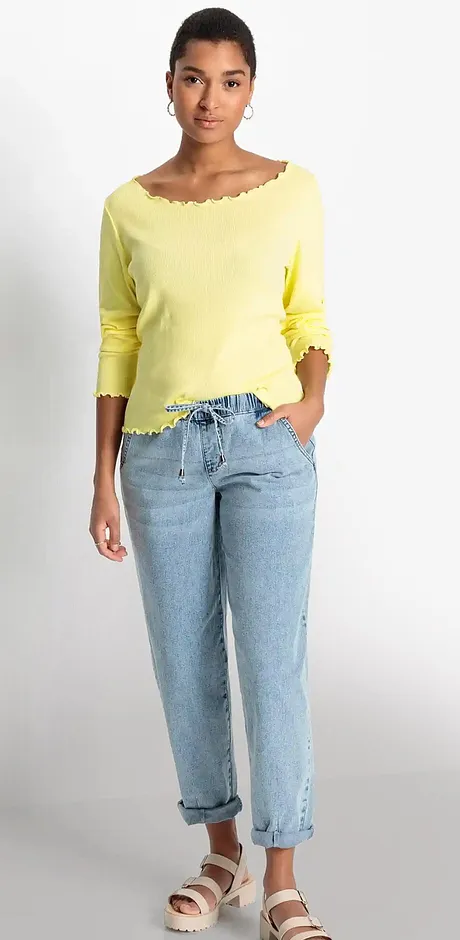 Tenue estivale : pull jaune à encolure bardot, jean bleu clair décontracté et sandales confortables.