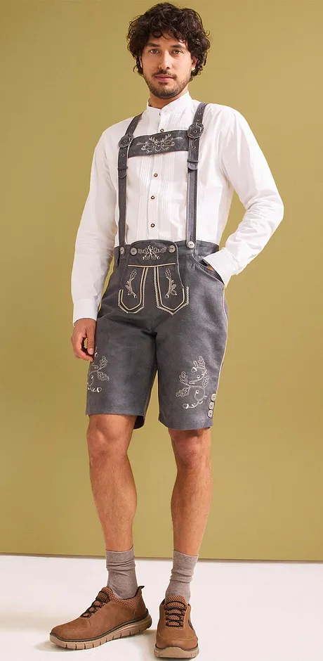 Weißes Hemd, graue Lederhosen mit Hosenträgern, kurze Socken und braune Schuhe.