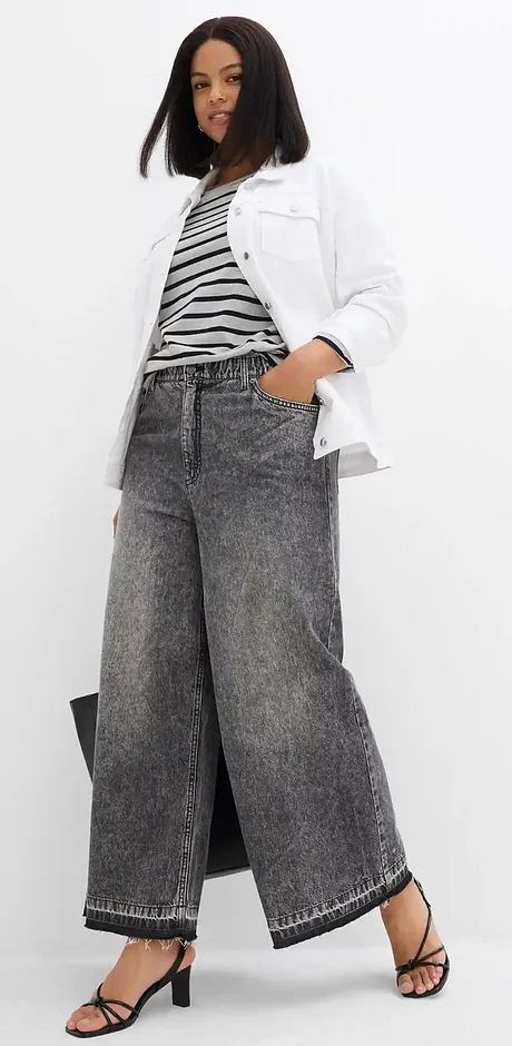 Weite Jeans, gestreiftes Top und weiße Jacke bilden einen lässigen, modernen Look.