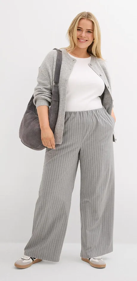 Graue Strickjacke mit weißem Top und gestreifter grauer Hose. 