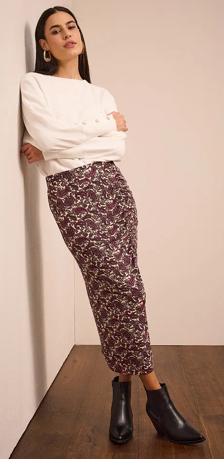 Pull en maille blanc, jupe longue à motifs et bottines noires. 