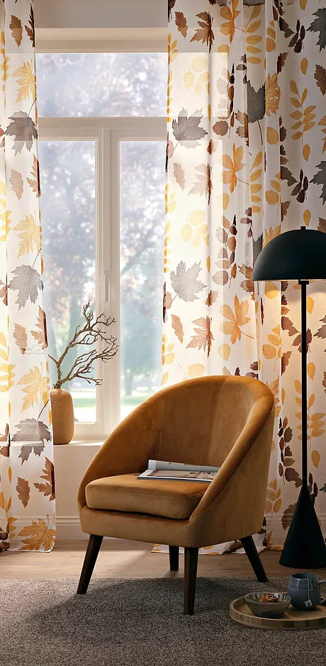 Herbstliche Vorhänge umrahmen das Fenster, während ein Sessel in Senfgelb den Raum schmückt.