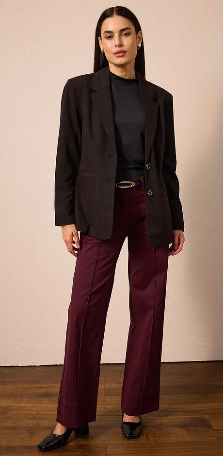 Blazer noir, pull foncé à col roulé et pantalon de couleur bordeaux.