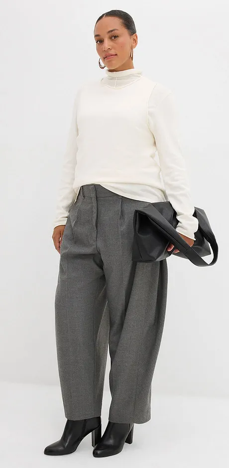Pull à col roulé couleur crème associé à un pantalon large gris et des bottes noires.