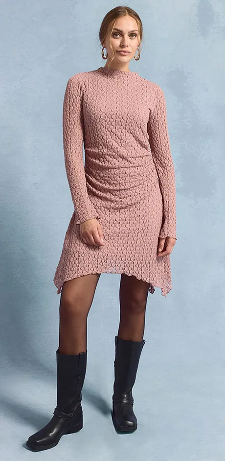 Robe en dentelle couleur rosé à manches longues associée à une paire de bottes noires.