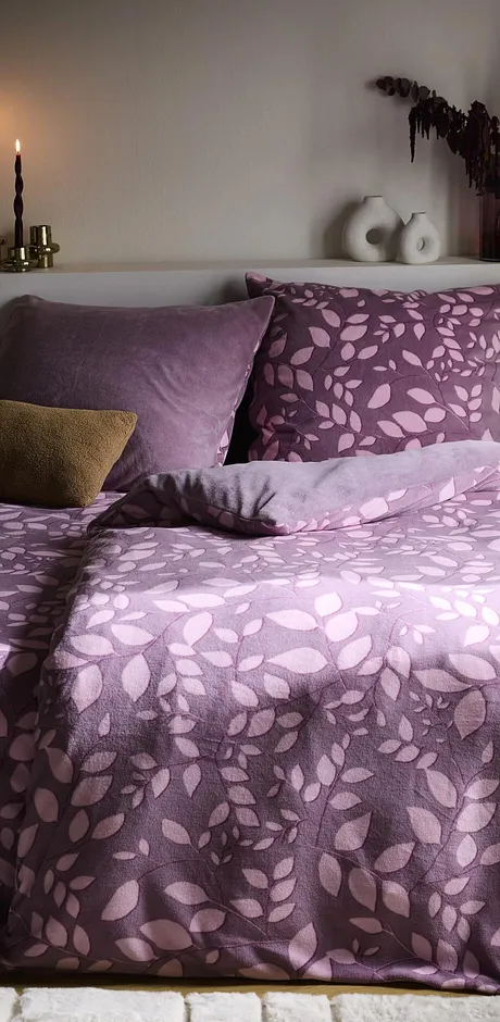 Une parure de lit confortable dans les tons lilas avec un motif floral décore la chambre à coucher.