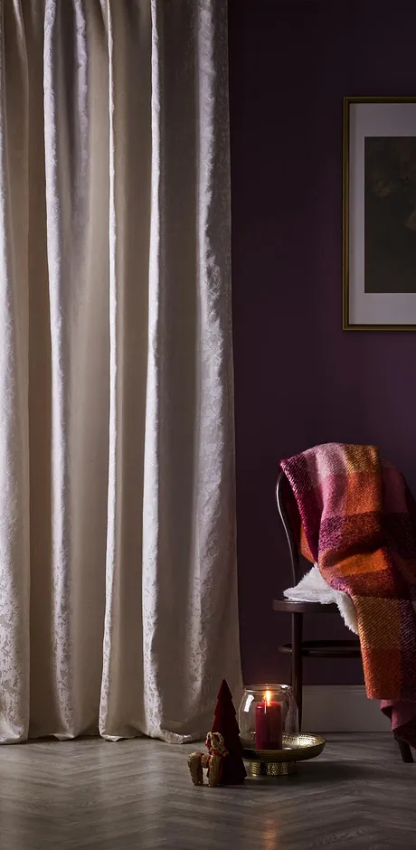 Fenêtre habillée d'un rideau de couleur claire. Une couverture dans des tons chauds est posée sur une chaise.