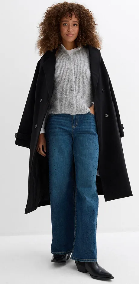 Manteau noir sur un pull en maille gris, associé à un jean large.