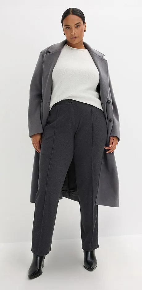 Manteau gris par dessus un pull blanc et un pantalon foncé.