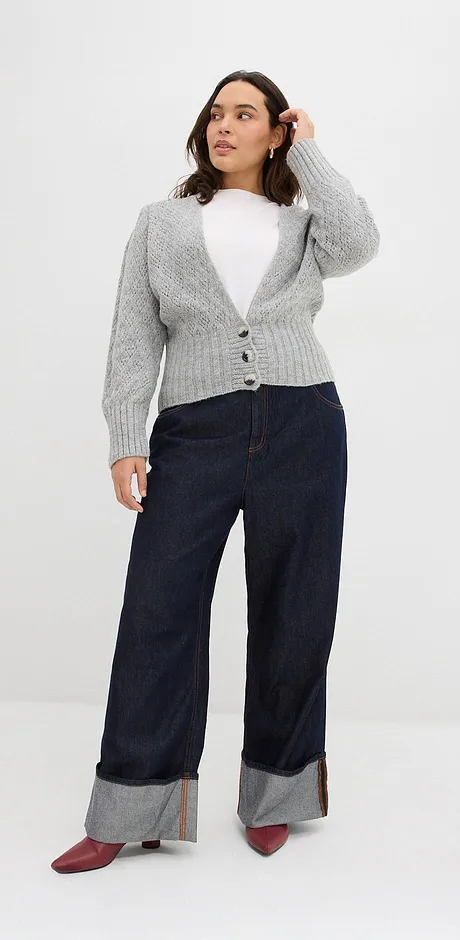 Cardigan gris en maille sur un top blanc, jean foncé avec grand revers et chaussures rouges.