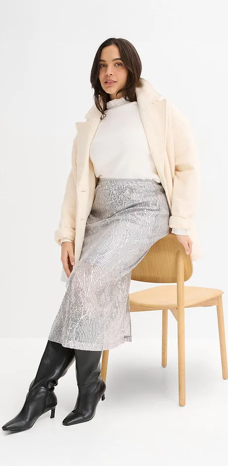 Manteau couleur crème, pull à col roulé blanc, jupe argentée et bottes noires.