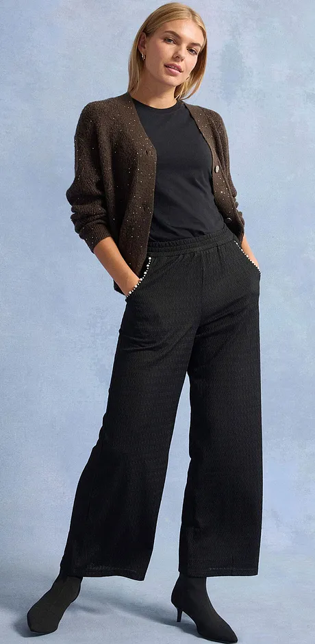 Schwarzer Hose, T-Shirt und glitzernde Strickjacke.