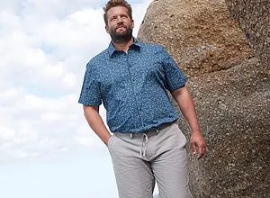 Chemise bleue à motifs et manches courtes, et pantalon clair.