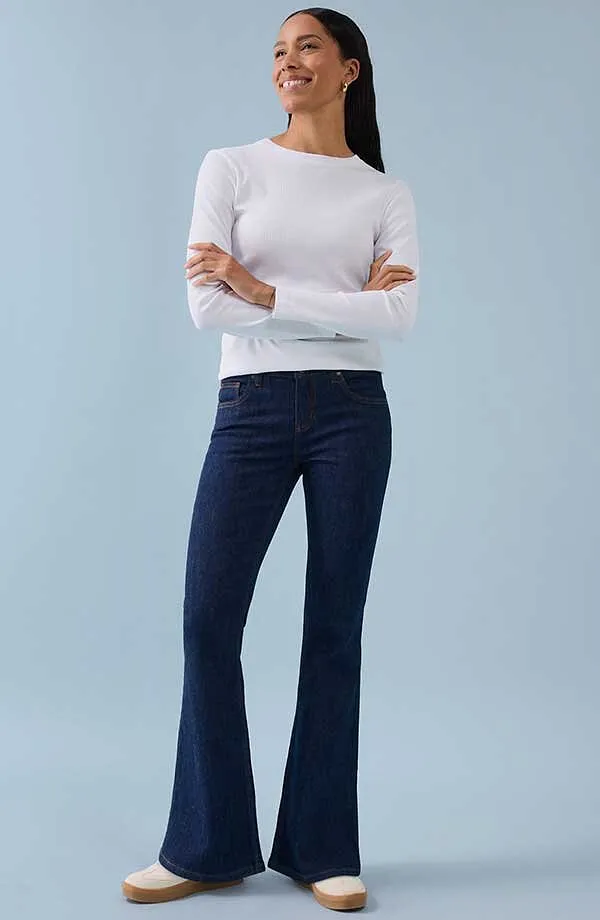 Weißes Langarmshirt kombiniert mit dunkelblauen Schlaghosen für einen zeitlosen, eleganten Look.