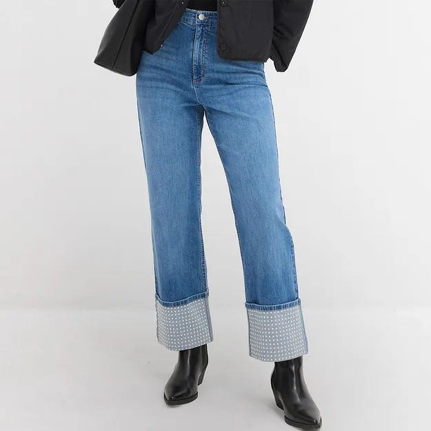 Blaue Jeans mit kariertem Umschlag, schwarze Stiefel und ein dunkler Blazer kombiniert.