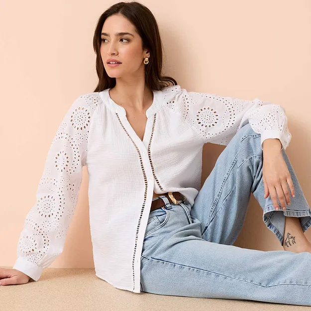 Wei&szlig;e Lochstickerei-Bluse mit langen &Auml;rmeln, kombiniert mit hellblauen Jeans und einem G&uuml;rtel.