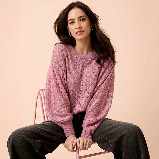 Weicher rosa Strickpullover mit Zopfmuster, kombiniert mit einer dunklen, weiten Jeans.