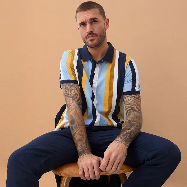 Polo ray&eacute; avec col bleu fonc&eacute;, associ&eacute; &agrave; un pantalon de couleur fonc&eacute;e.