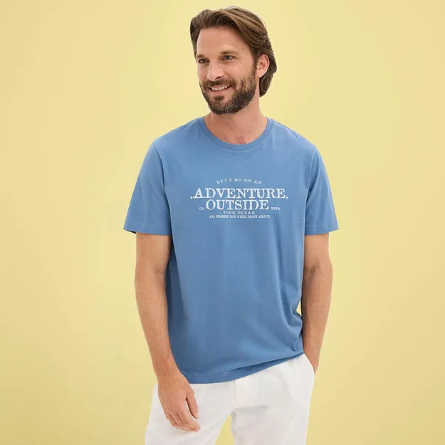 Mann tr&auml;gt ein l&auml;ssiges blaues T-Shirt mit wei&szlig;em Aufdruck und helle Hose.