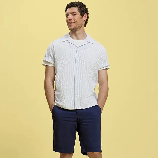 Un homme v&ecirc;tu d'une chemise blanche &agrave; manches courtes et d'un short bleu fonc&eacute;.