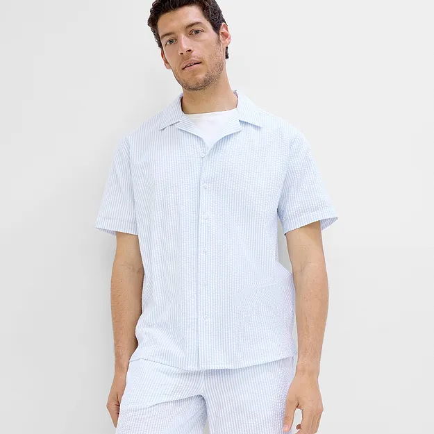 Un homme v&ecirc;tu d'une chemise &agrave; manches courtes ray&eacute;e blanc et bleu clair et d'un short assorti.