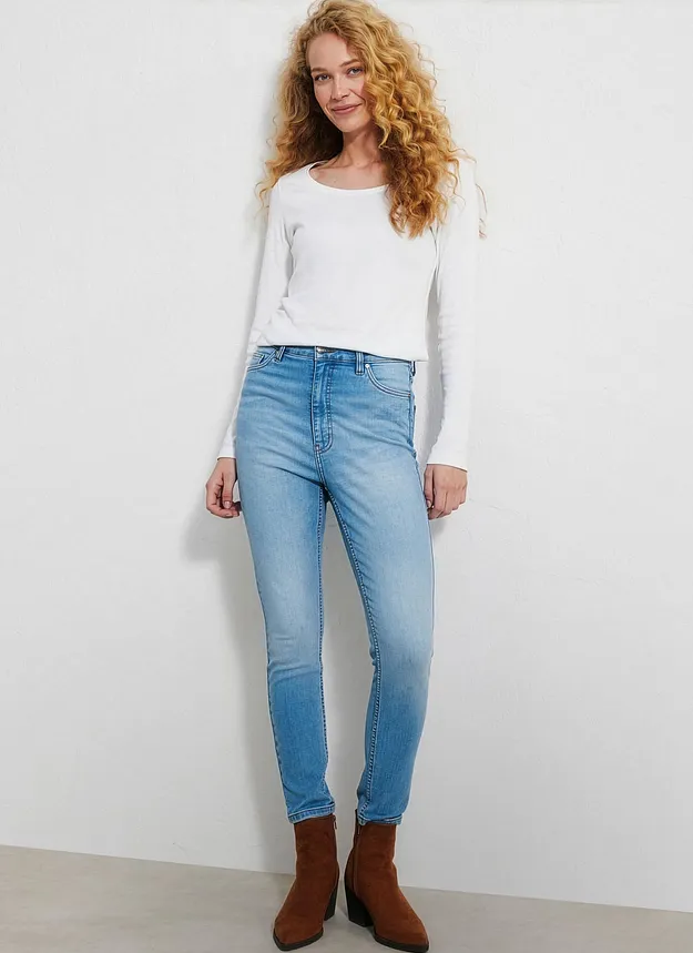 Une femme v&ecirc;tue d'un T-shirt blanc basique, un jean clair et des bottines marron.
