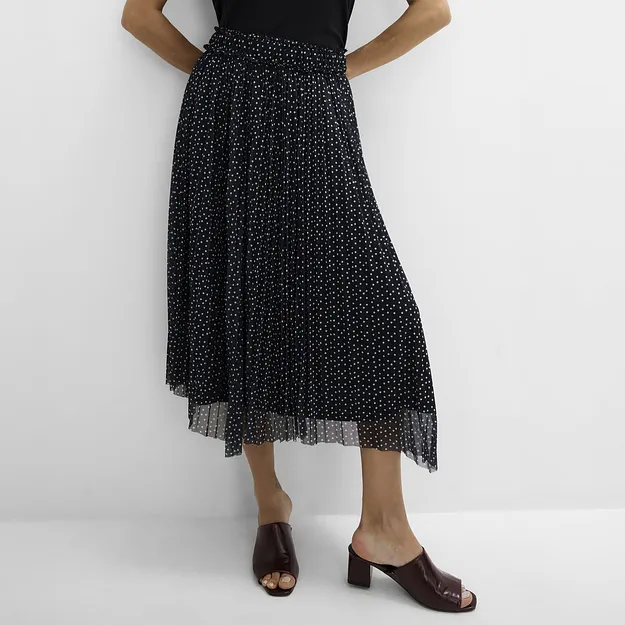 Schlichtes schwarzes Top, gepunkteter Plisseerock und elegante dunkelbraune Pantoletten.