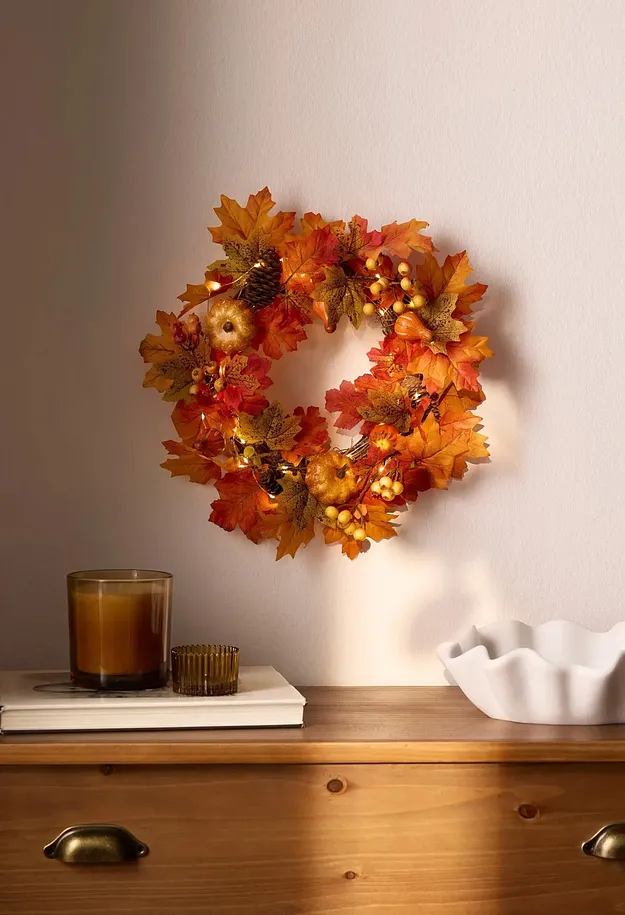 Wand ziert ein beleuchteter Herbstkranz. Kerzenlicht und eine Schale auf dem Holztisch.