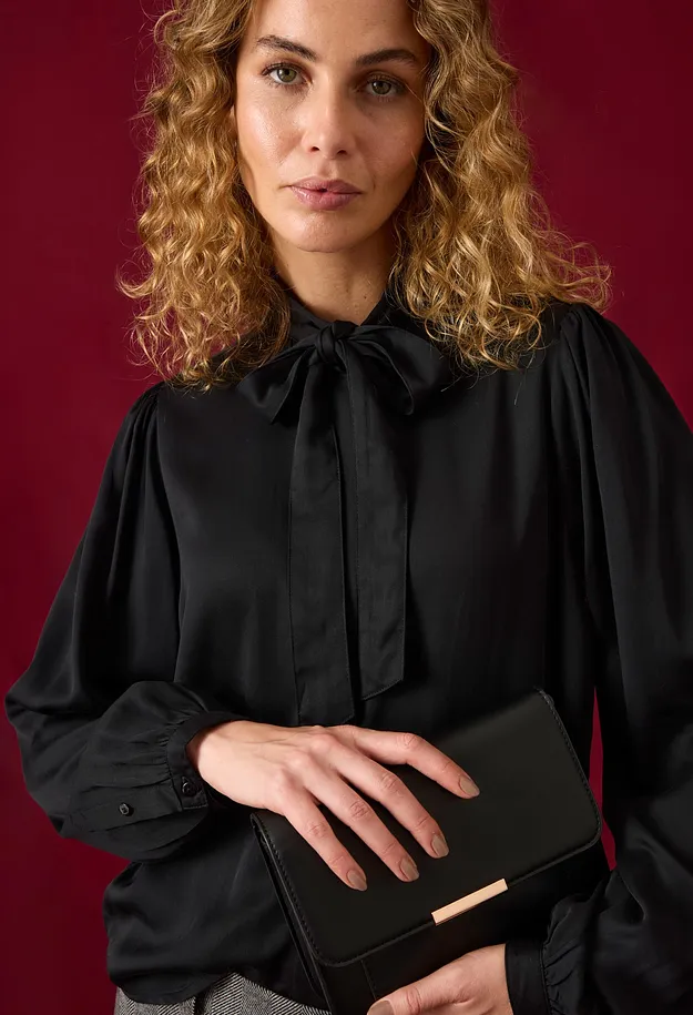 Schwarze Bluse mit eleganter Schleife und weiten &Auml;rmeln, dazu eine schicke Clutch.
